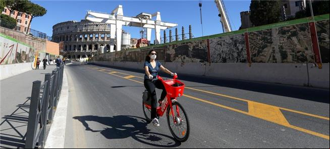 Ciclista de máscara pedala perto do Coliseu em Rom